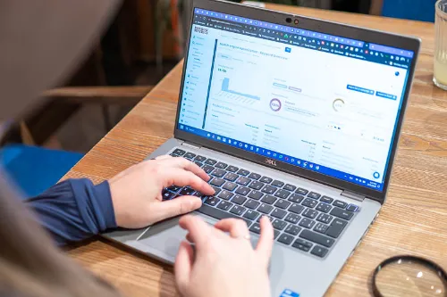 Notebook s grafy, na stole položenou lupou a pracujícím člověkem