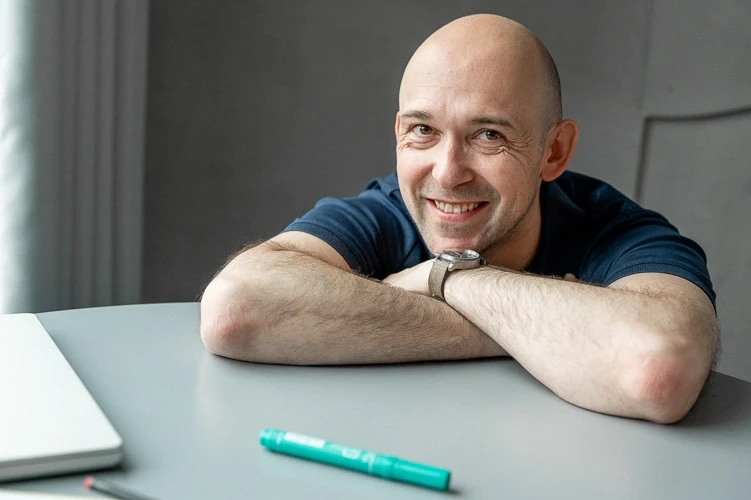 Usmívající se muž opřený o stolek s položenou zelenou fixou